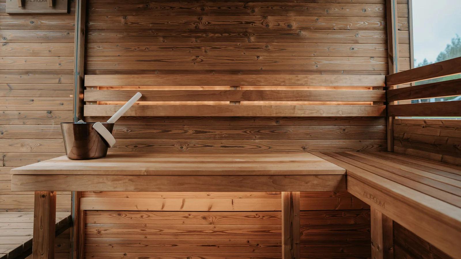 Official Auroom photograph of a wooden sauna interior with bucket and ladle